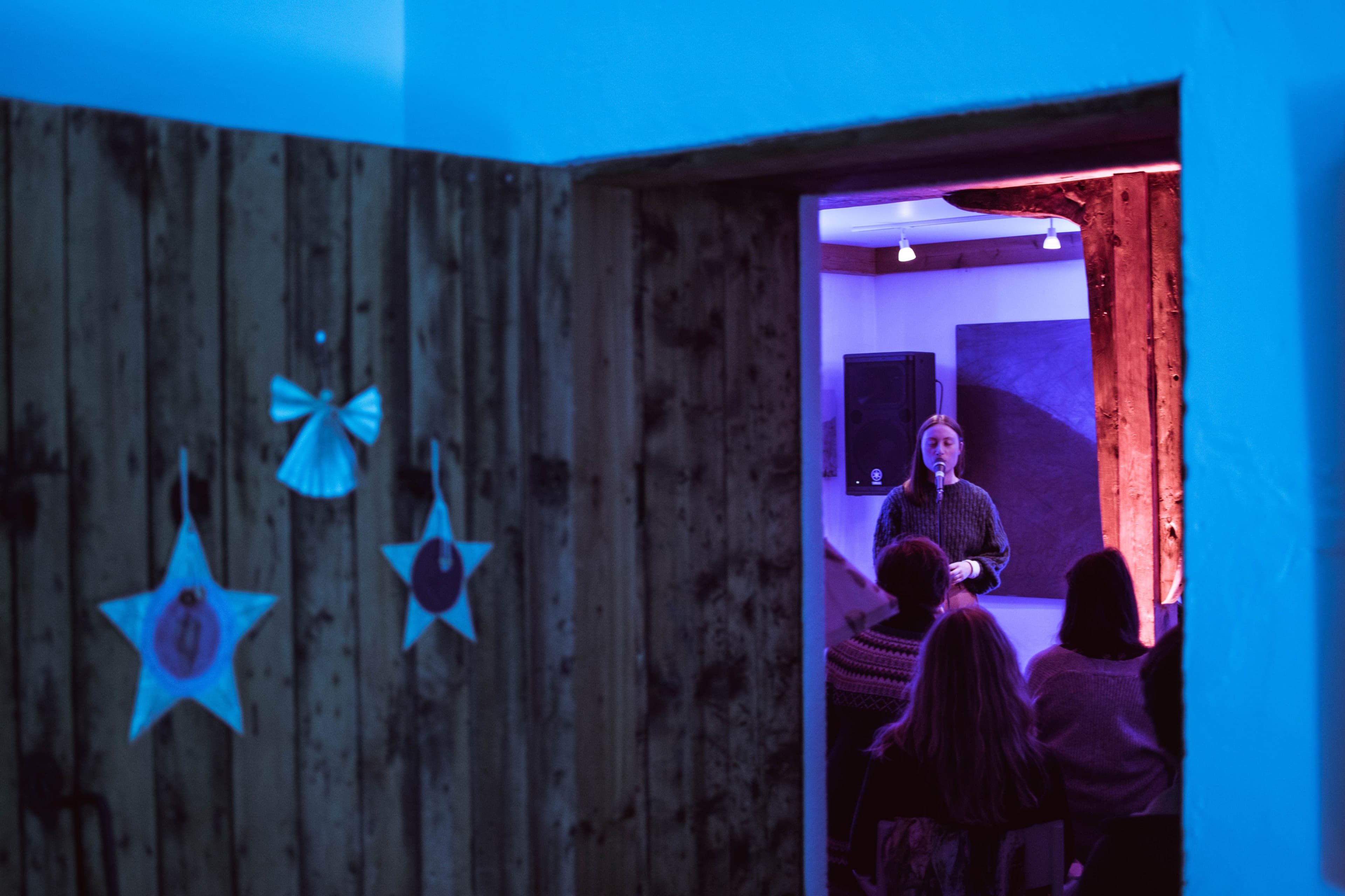 En kvinnlig vokalist som synger, sett gjennom en døråpning, med en massiv tredør i forgrunnen