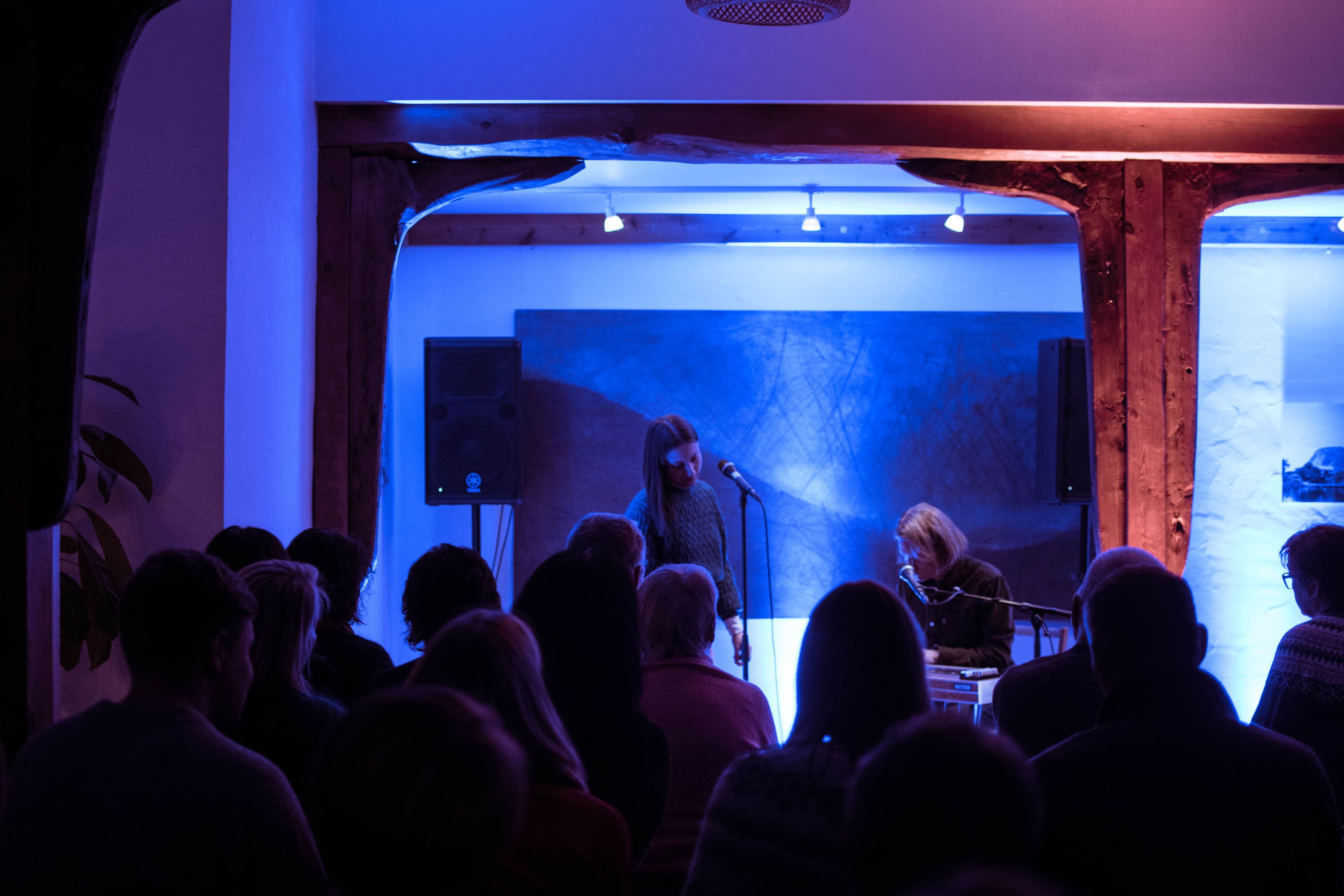 Kvinnlig vokalist og mannlig gitarist i dempet lokale, med publikummere i forgrunnen