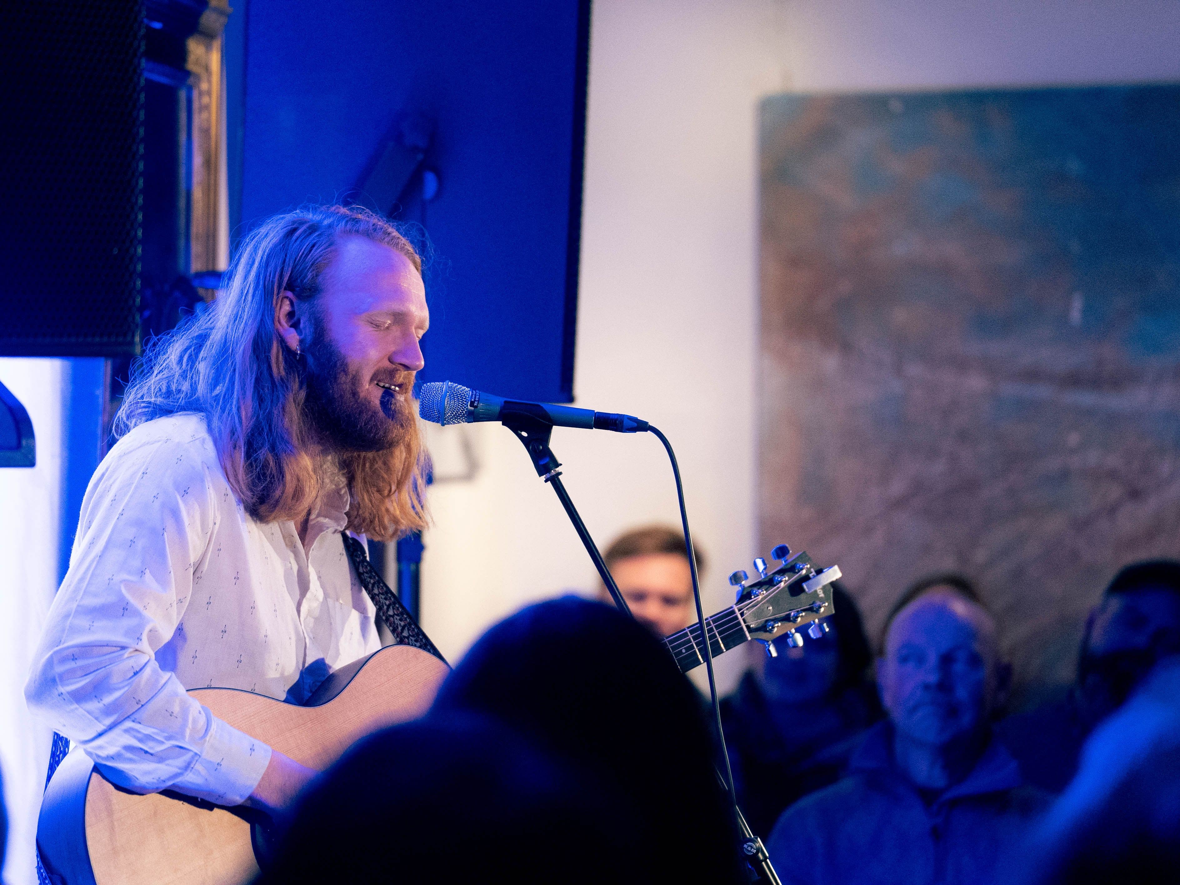 Mannlig artist som synger og spiller gitar med lukkede øyne, omringet av publikummere
