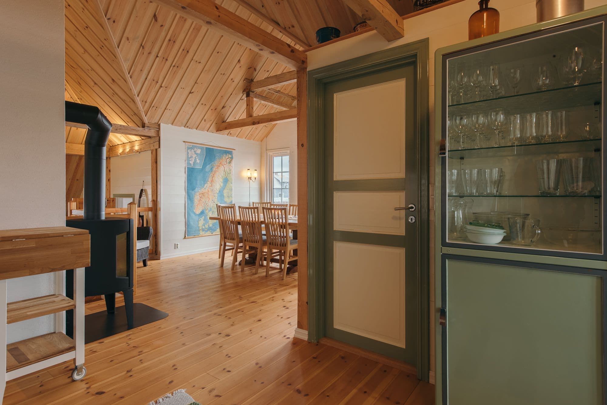 Åpent rom med grønt skap i forgrunnen, og bord og stoler i bakgrunnen